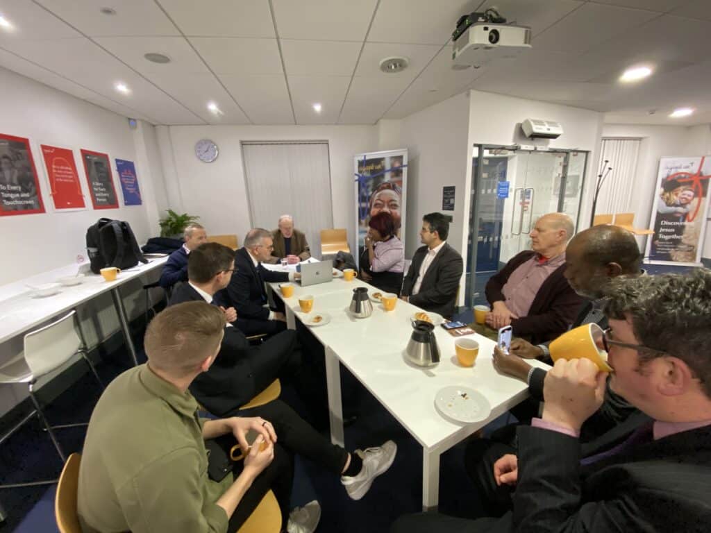 A group of legal professionals sitting around a table, drinking coffee and listening to a speaker.